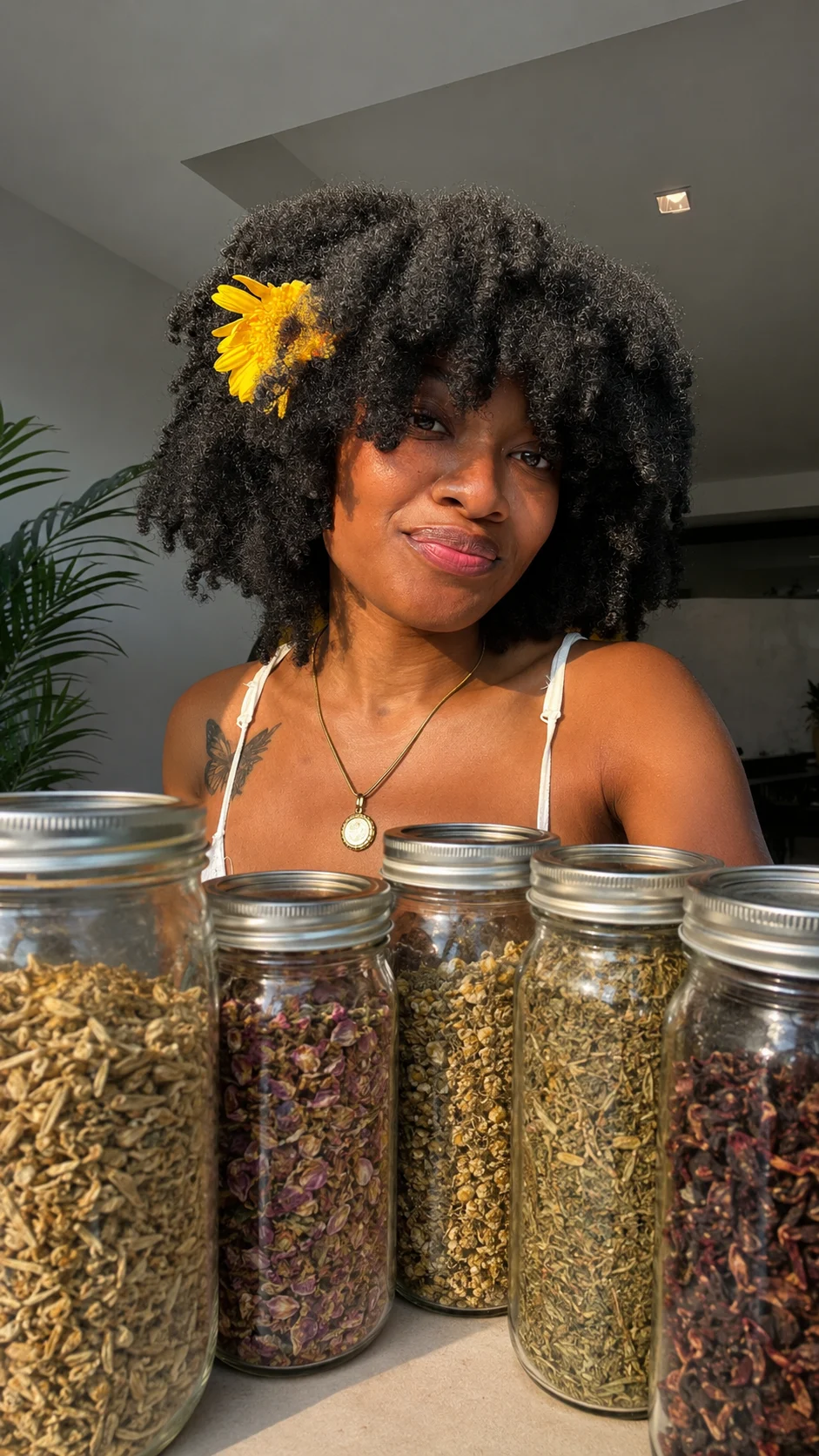 Maleeah Jay with a yellow flower in her hair, behind jars of dried herbs