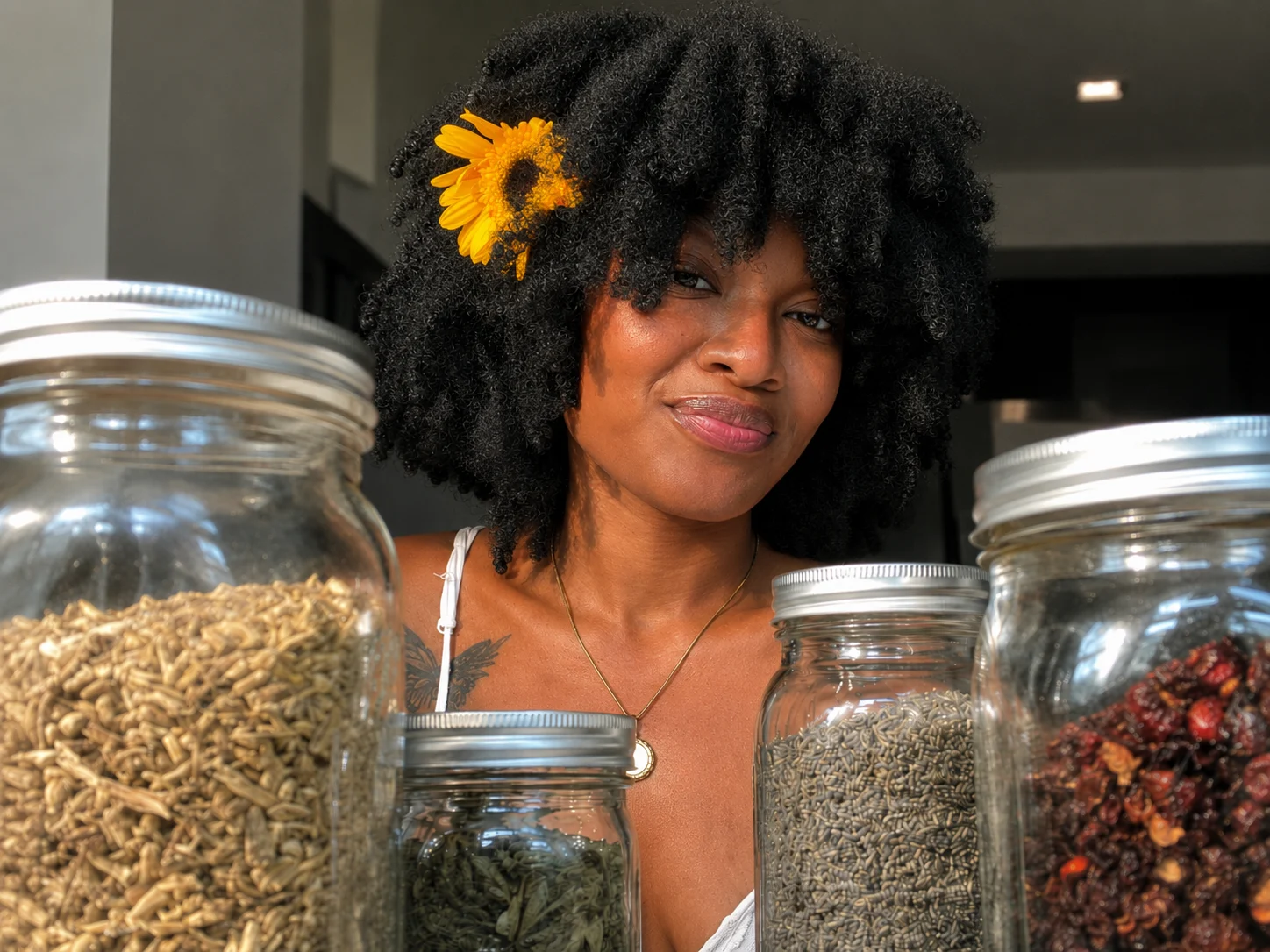 Maleeah Jay with a yellow flower in her hair, behind jars of dried herbs