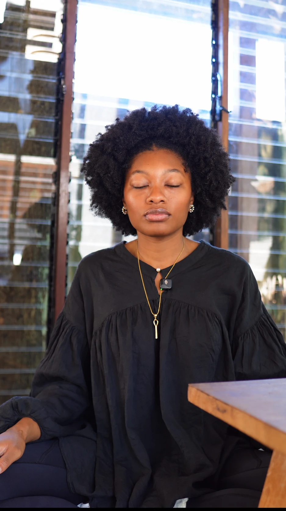 Maleeah Jay in a black shirt, seated with her eyes closed, meditating by a window